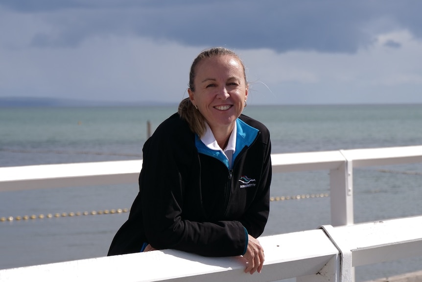 Lisa Shreeve lehnt sich lächelnd an ein Geländer des Stegs, das Meer im Rücken.