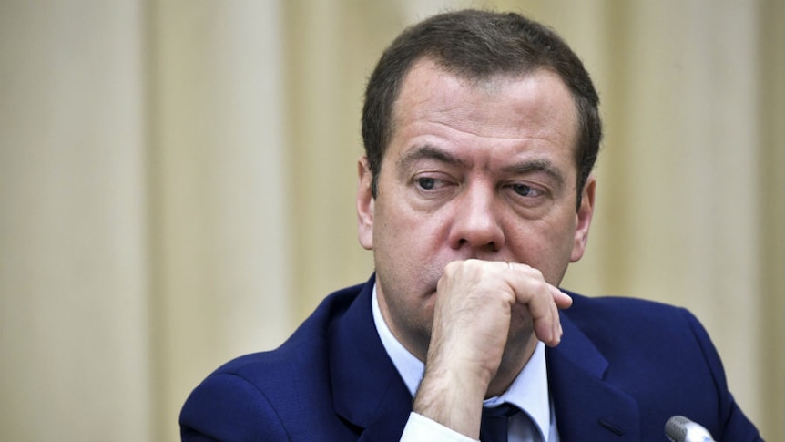 Head and shoulders shot of Dmitry Medvedev sitting at a microphone with his hand in front of his mouth.