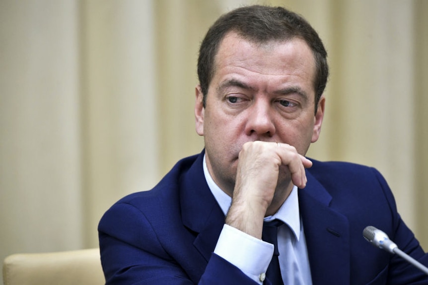 Head and shoulders shot of Dmitry Medvedev sitting at a microphone with his hand in front of his mouth.