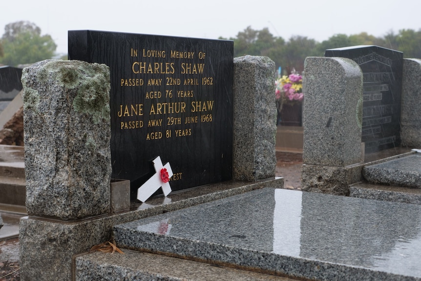 A small white cross with a poppy on it leaning against a grave headstone