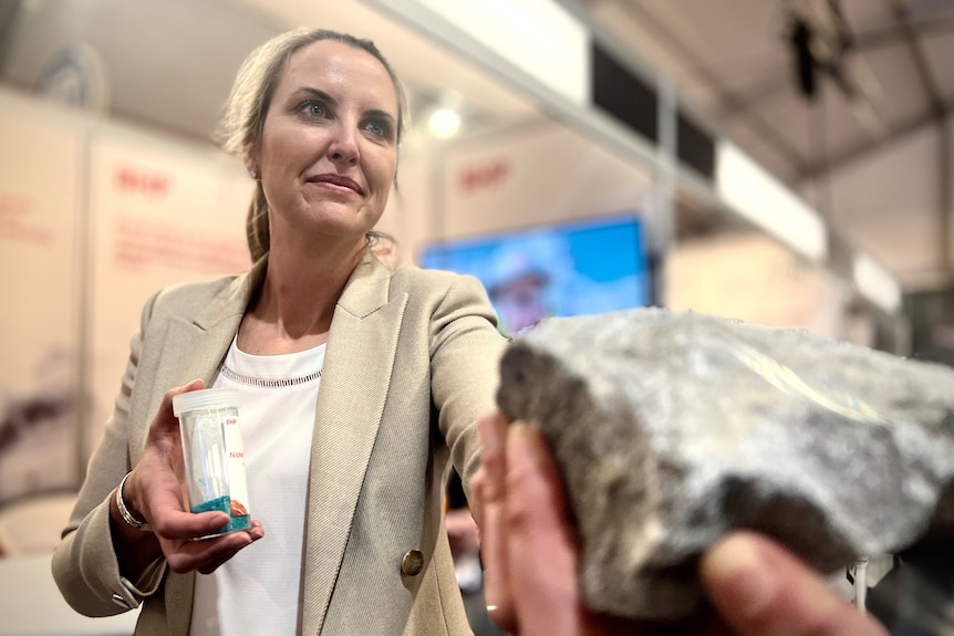 A woman wearing a white jacket holds a nickel rock.