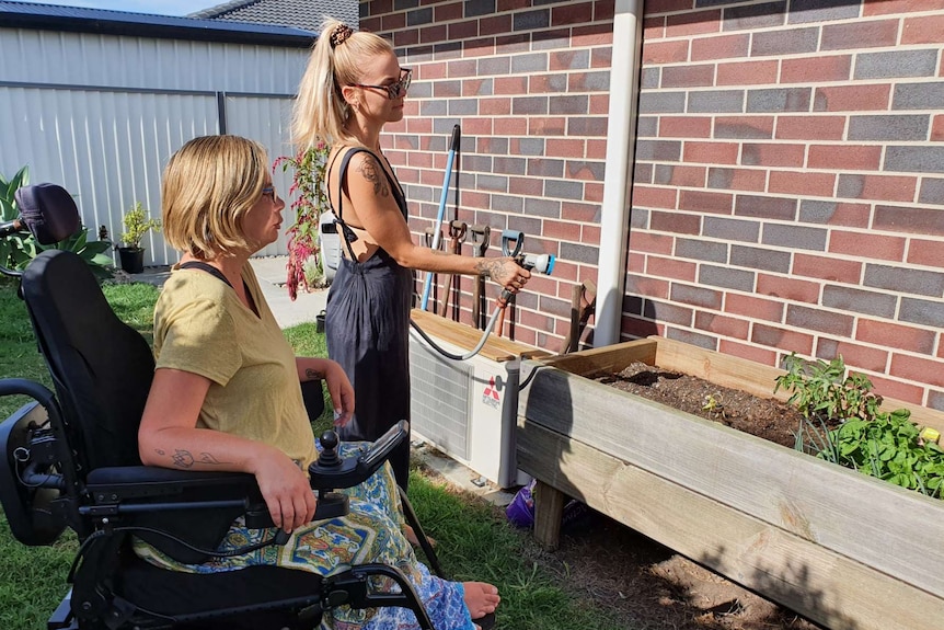 A woman uses a hose to water a patch of garden as Kelly Cox watches on.