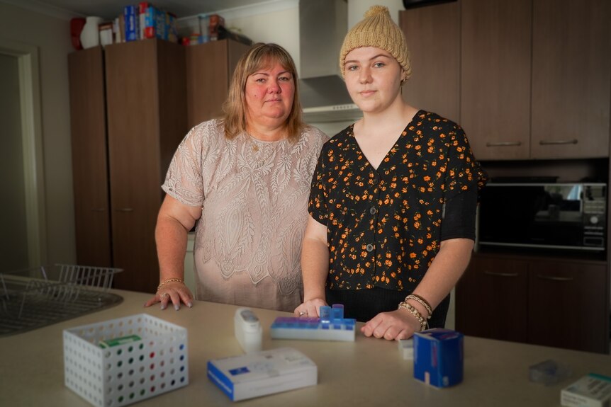 a mother and her daughter standing in a kitchen with medications on the table