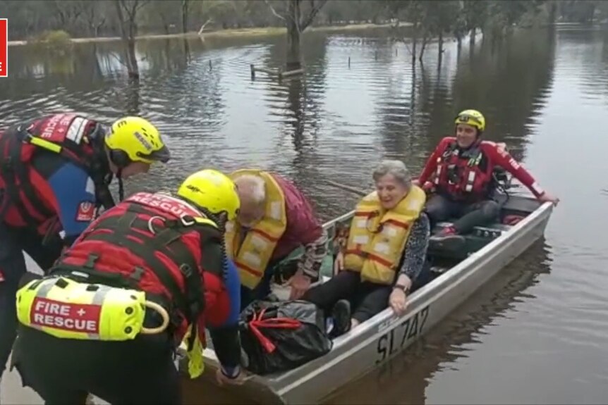 Firefighters pushing a tin boat in flood water with an elderly couple
