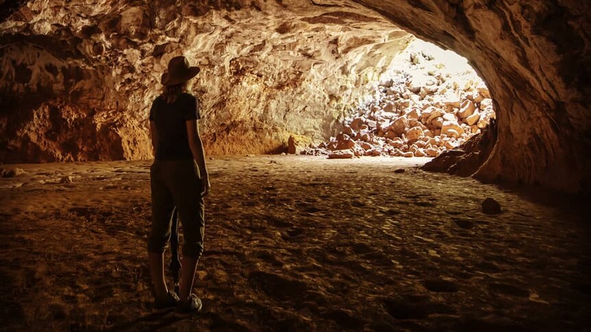 A person stands at the entrance to a cave, as light streams in.