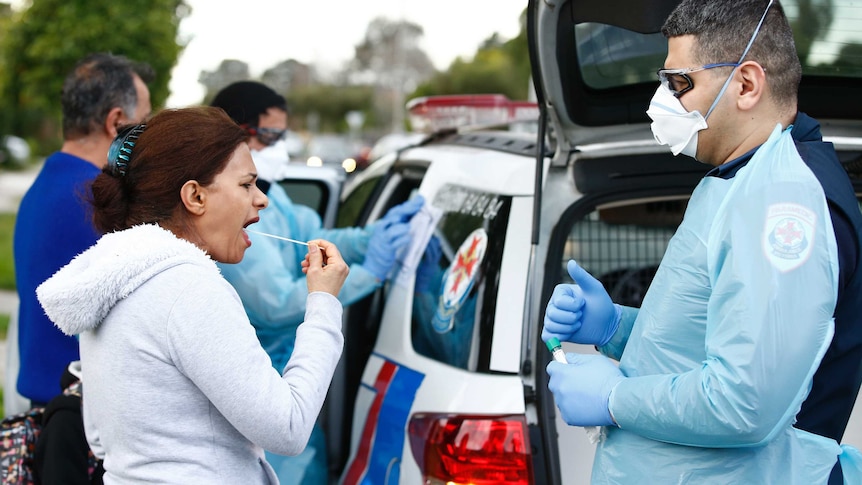 A woman holds a swab to her mouth as an ambulance officer watches.