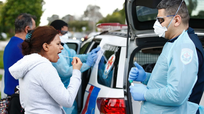 A woman holds a swab to her mouth as an ambulance officer watches.