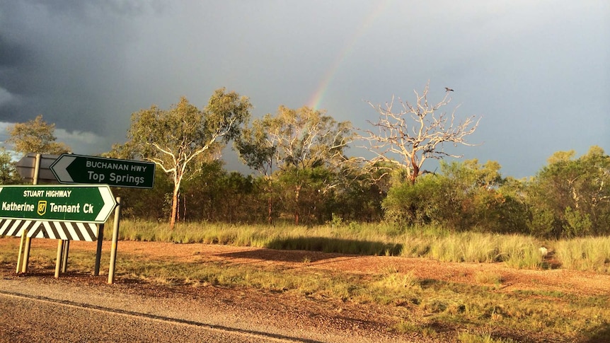 A stormy sky above a road sign pointing to Tennant Creek.