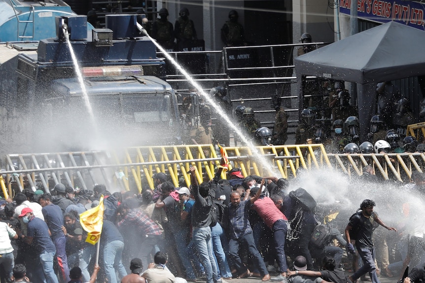 Police use water cannons against demonstrators behind a barrier.