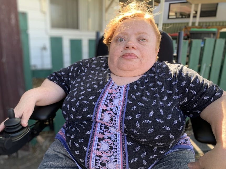 A middle-aged, ginger-haired woman who lives with brittle bone disease sitting in a motorised wheelchair.