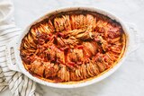 Bright red tomatoey potato gratin in a white baking dish. The sweet potato slices are stacked vertically in a neat pattern.
