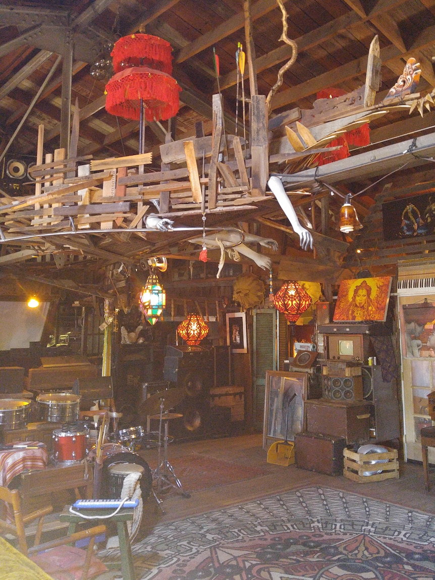 The wooden interior of a converted wooden warehouse covered in art, mannequin hands and bohemian lamps.