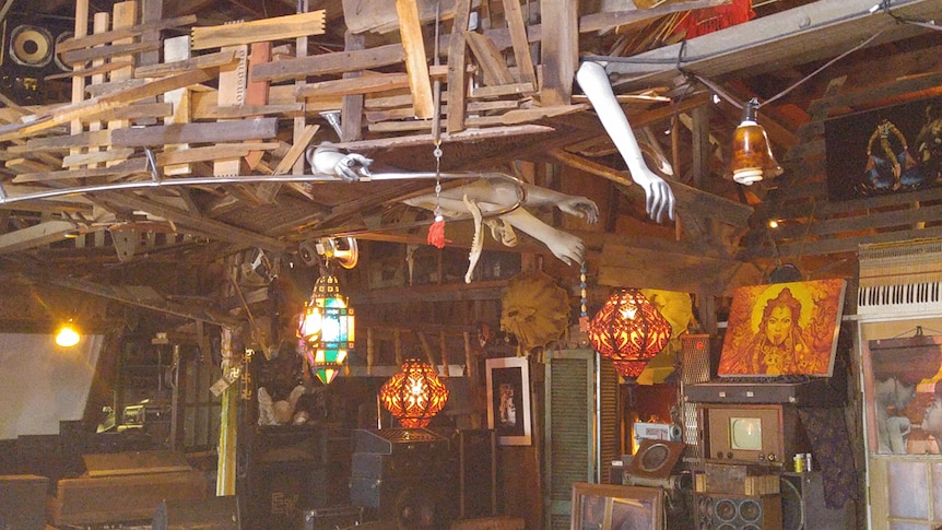 The wooden interior of a converted wooden warehouse covered in art, mannequin hands and bohemian lamps.