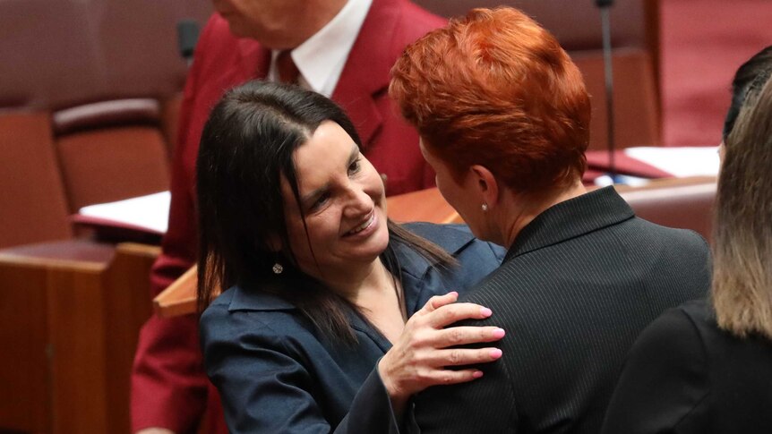 Jacqui Lambie smiles while hugging Pauline Hanson in the Senate. Senator Lambie has pink nail polish on her fingers