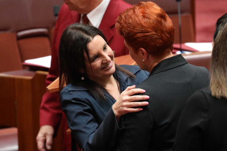 Jacqui Lambie smiles while hugging Pauline Hanson in the Senate. Senator Lambie has pink nail polish on her fingers