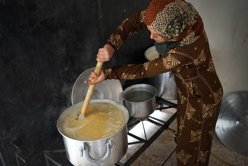 A woman stirring a huge pot of lentils