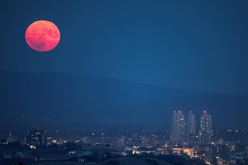 A red, full moon rises above a city 