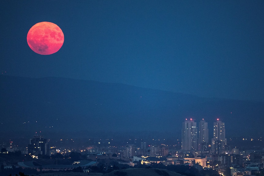 A red, full moon rises above a city 