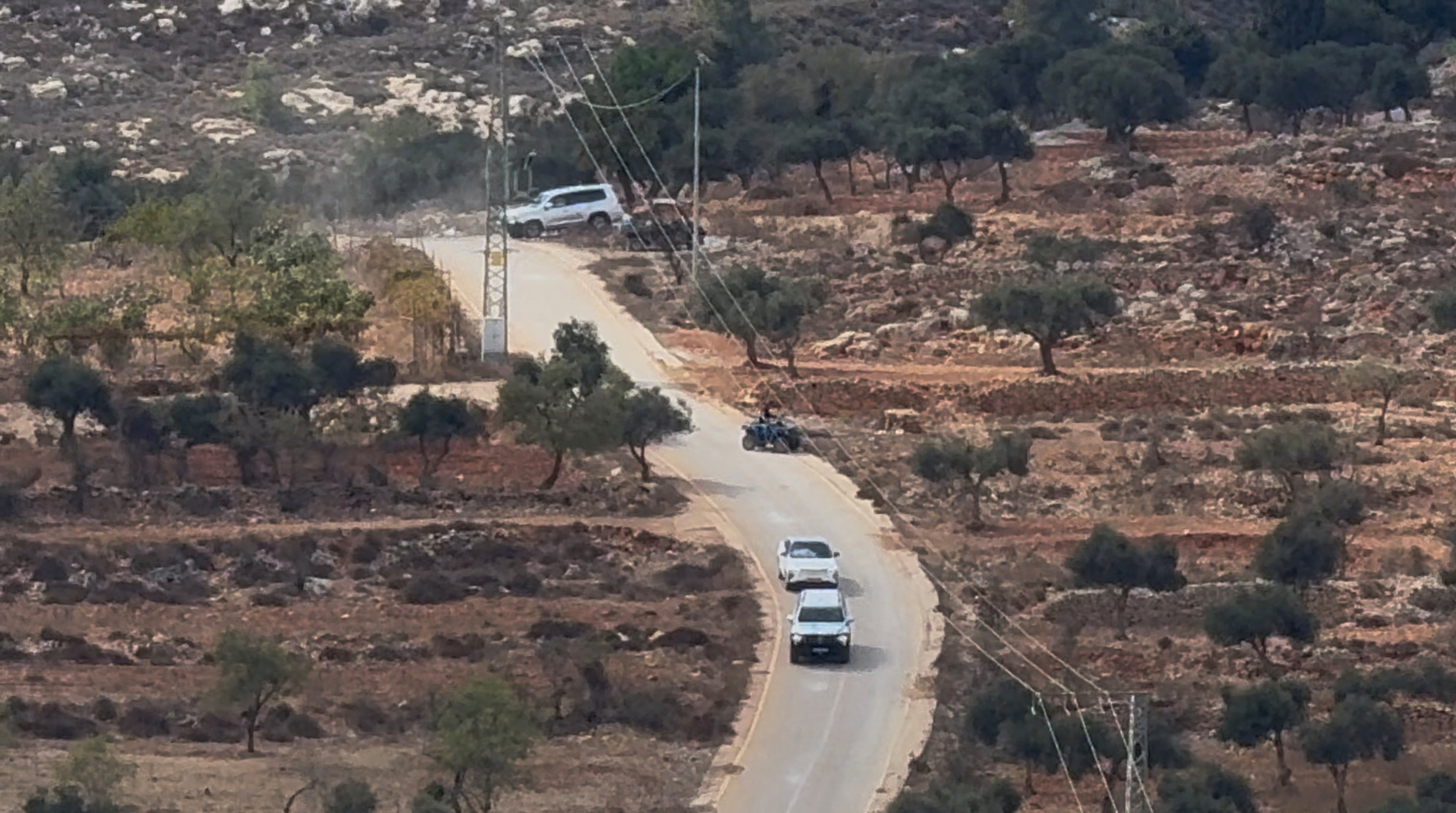 A zoomed in landscape image of a road in dry countryside, multiple vehicles and a motorbike drive down a road