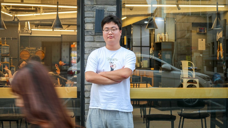 A South Korean man in a Popeye t-shirt stands in front of a cafe.