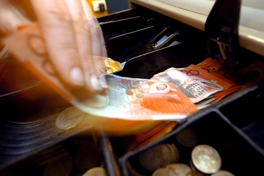 A shop assistant removes twenty dollar notes from a till