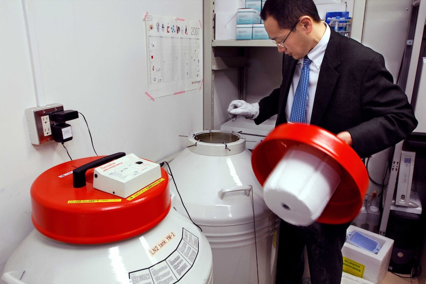 A man in a laboratory opens a large, refrigerated vat.