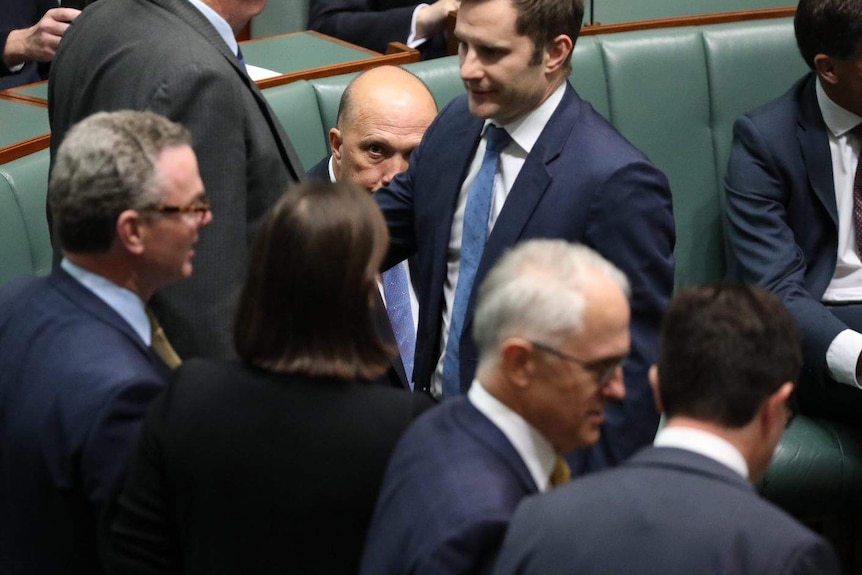 Peter Dutton sitting on the member's bench peers up at Mr Turnbull over the arm of a colleague. Turnbull is looking other way.