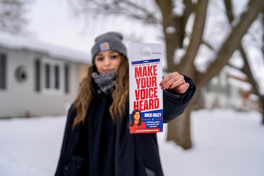 Yazmin holds a flyer that says 'make your voice heard' with Nikki Haley's face on it. She's outside in the snow.