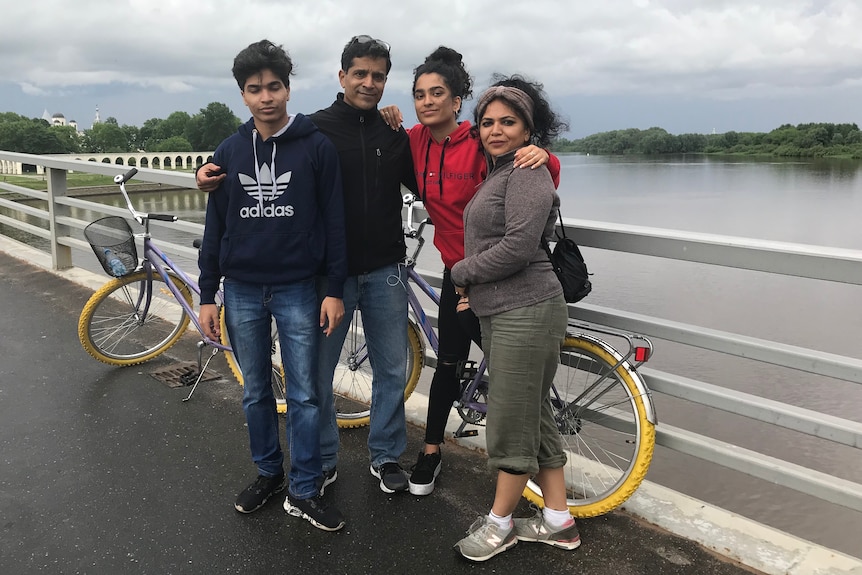 Jyoti Pande Lavarkare stands on a bridge over a body of water with grey skies with her husband and two children.