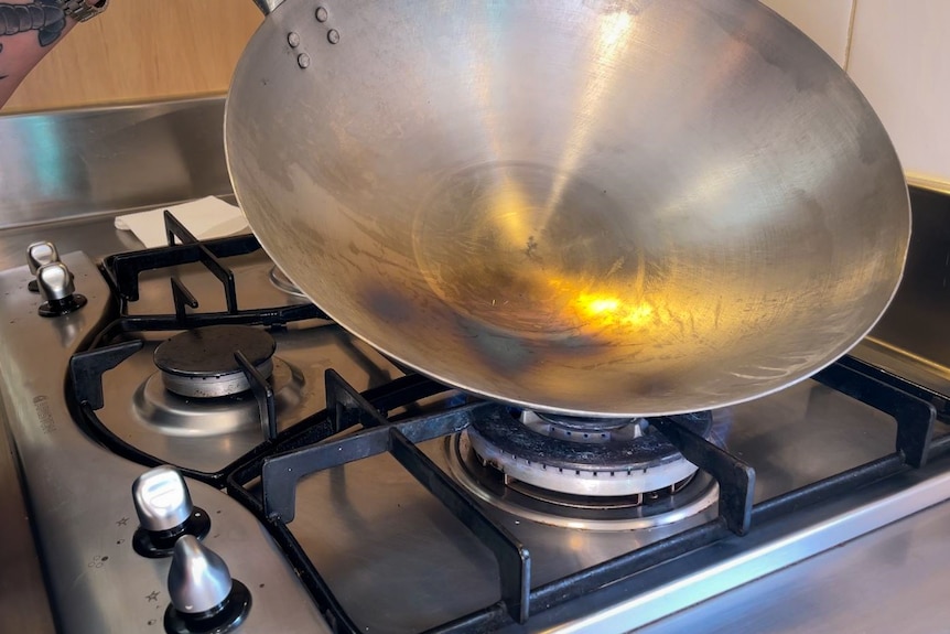 A silver wok on a gas flame, the carbon steel changing to a darker colour.