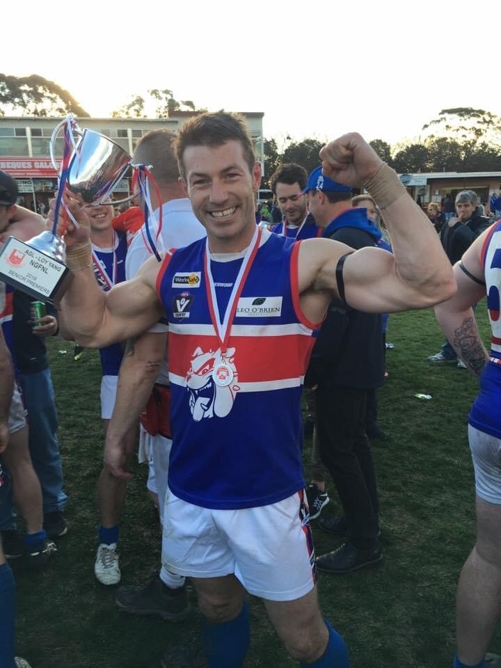 A man in football gear smiles and holds a silver cup in the air.