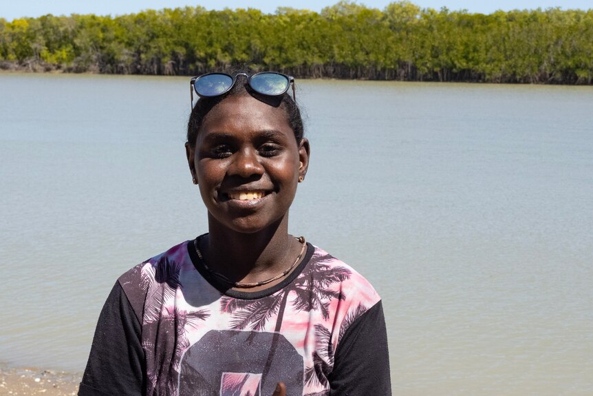 A young woman smiles, standing in front of a creek and mangroves