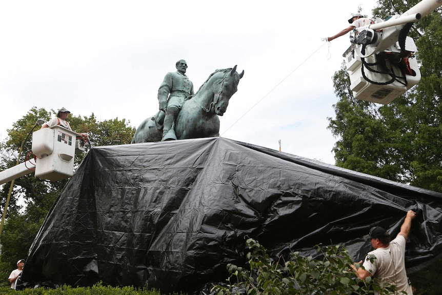 Workers lift tarp over a statue of Robert E Lee.