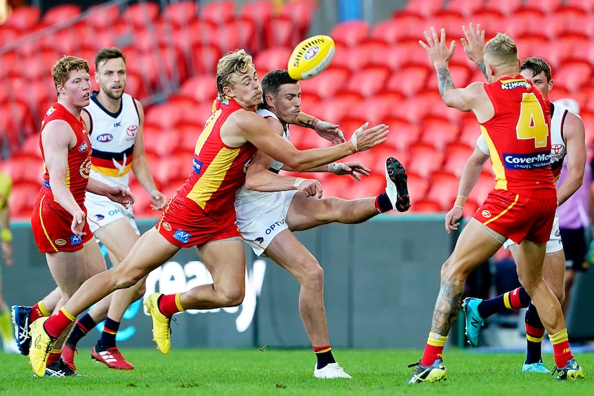 An AFL player hurriedly gets his boot to the ball as he is grabbed by an opponent.  