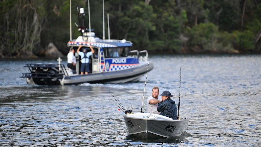 Fishermen in a dinghy travel down the Hawkesbury River with a police boat in the background.