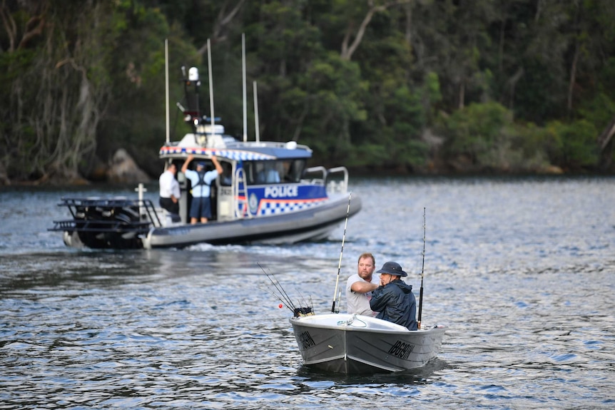 Fishermen in a dinghy travel down the Hawkesbury River with a police boat in the background.