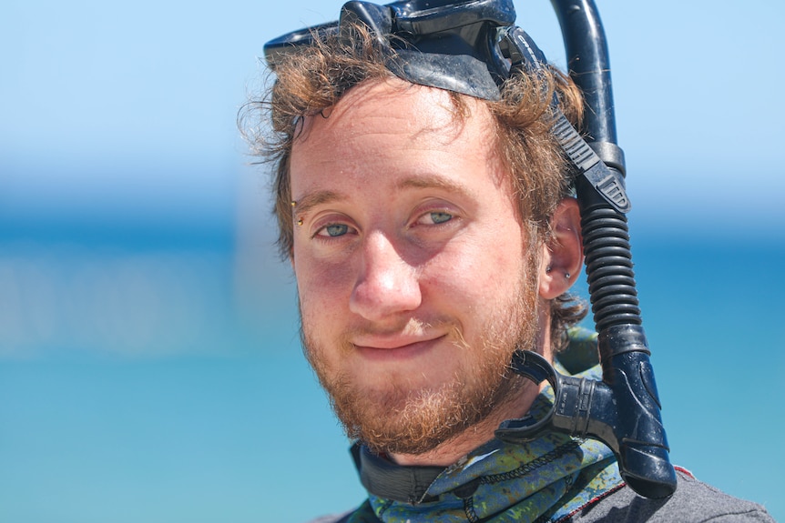 A young man smiles at the camera wearing a snorkel mask on his head.