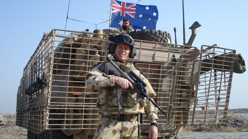 A soldier standing in front of a military vehicle with a rifle.
