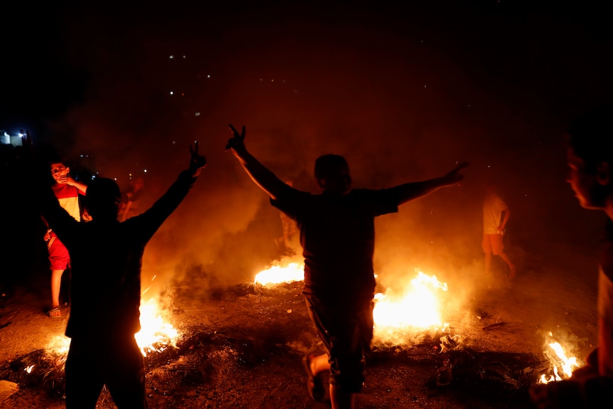 People stand in front of fires lit as part of a protest