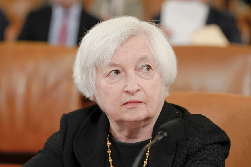 A woman with white hair, black clothes and a golden necklace is pictured looking out of frame.