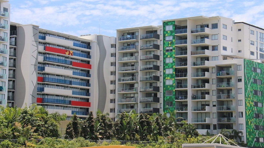 Row of apartment buildings with treetops in foreground along a street in Brisbane.