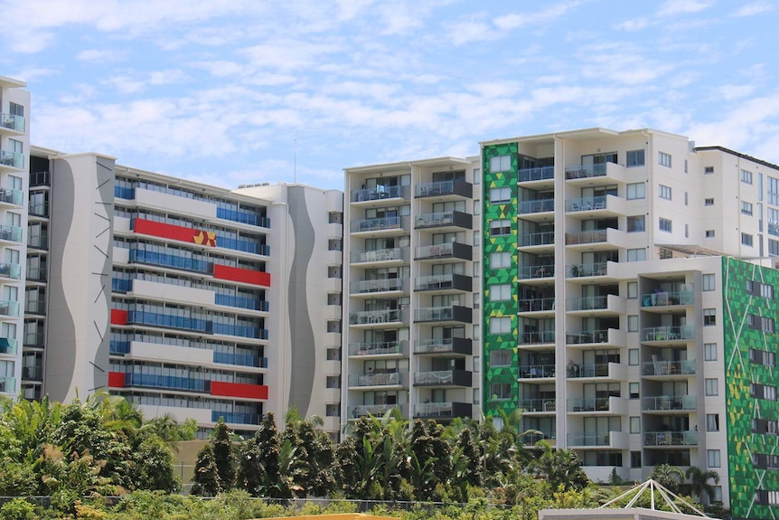 Row of apartment buildings with treetops in foreground along a street in Brisbane.