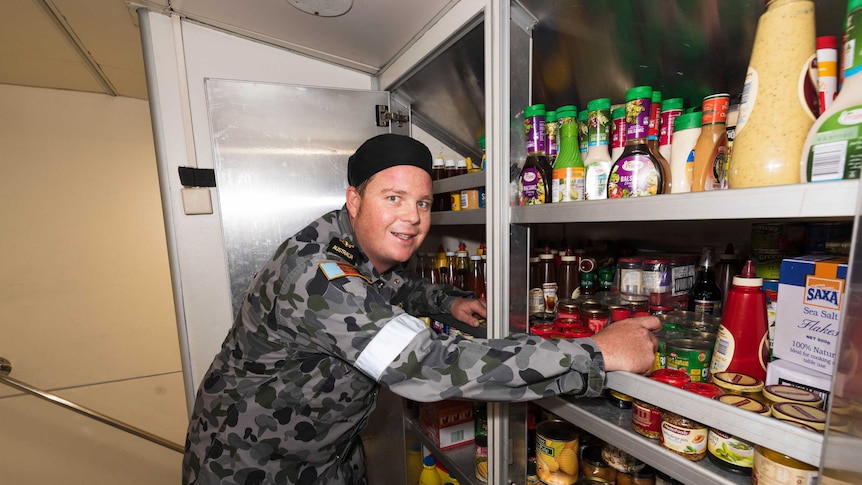 Defence force gentleman in camouflage uniform leaning into open pantry filled with food.