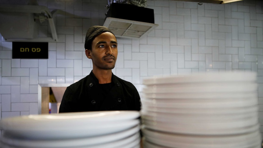 A man stands in a kitchen behind two piles of plates.