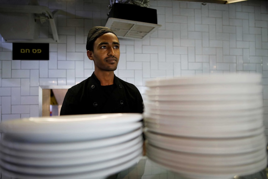 A man stands in a kitchen behind two piles of plates.