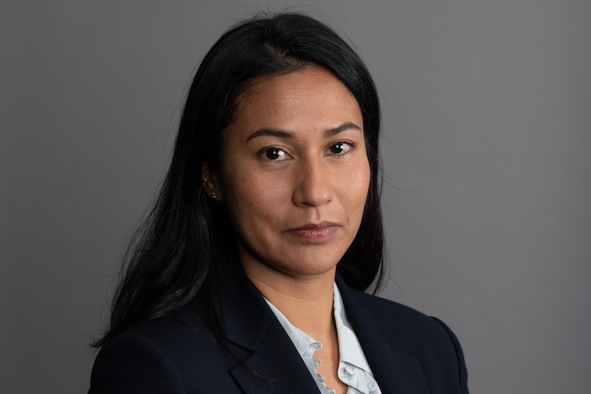 A headshot of a woman with long dark hari in a navy blazer. 