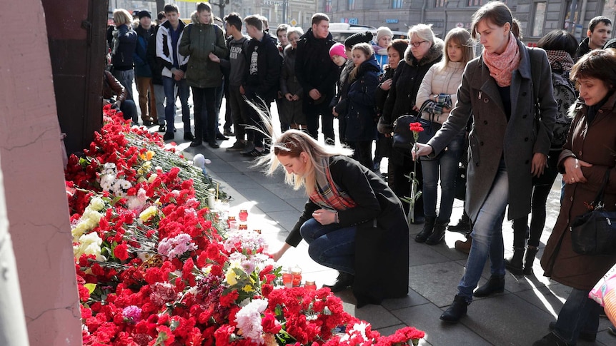 A woman lays flowers at a memorial outside Technological Institute while crowds of people watch on.