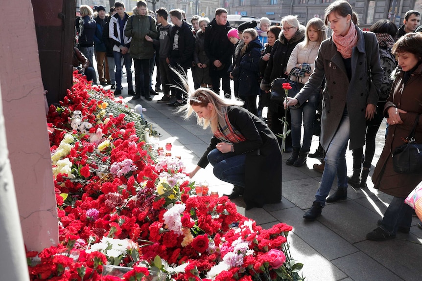 A woman lays flowers at a memorial outside Technological Institute while crowds of people watch on.
