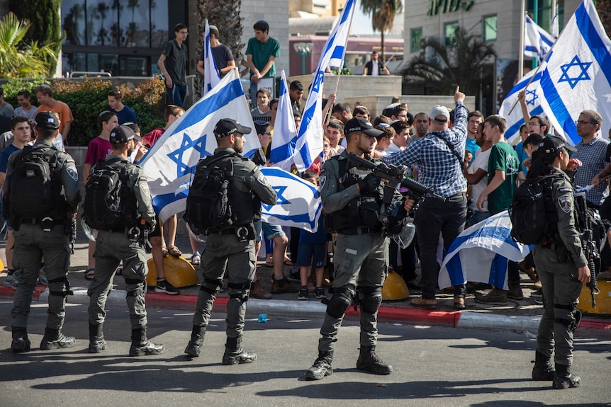 Israeli paramilitary border police officers stand guard in front of Jewish right-wing demonstrators.