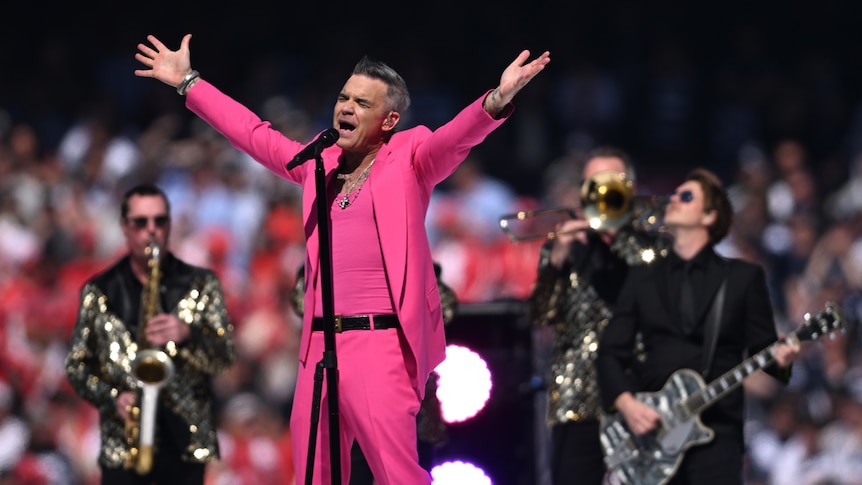 Singer Robbie Williams dressed in all one colour raises his arms in the air as he performs at the AFL Grand Final at the MCG.